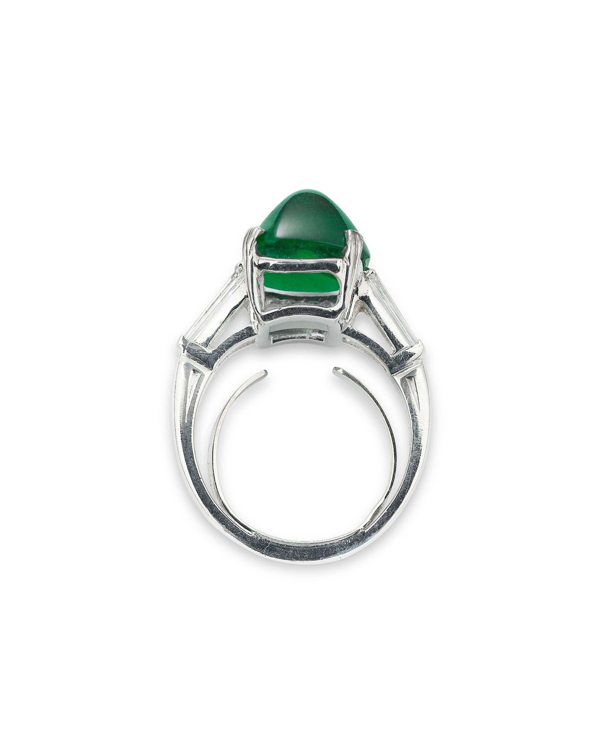This elegant ring by the renowned Oscar Heyman & Brothers showcases a fantastic sugar loaf emerald. Weighing 7.00 carats, this stunning gem's remarkable cut displays its verdant hue flawlessly. Flanked by two channel-set diamonds weighing .40