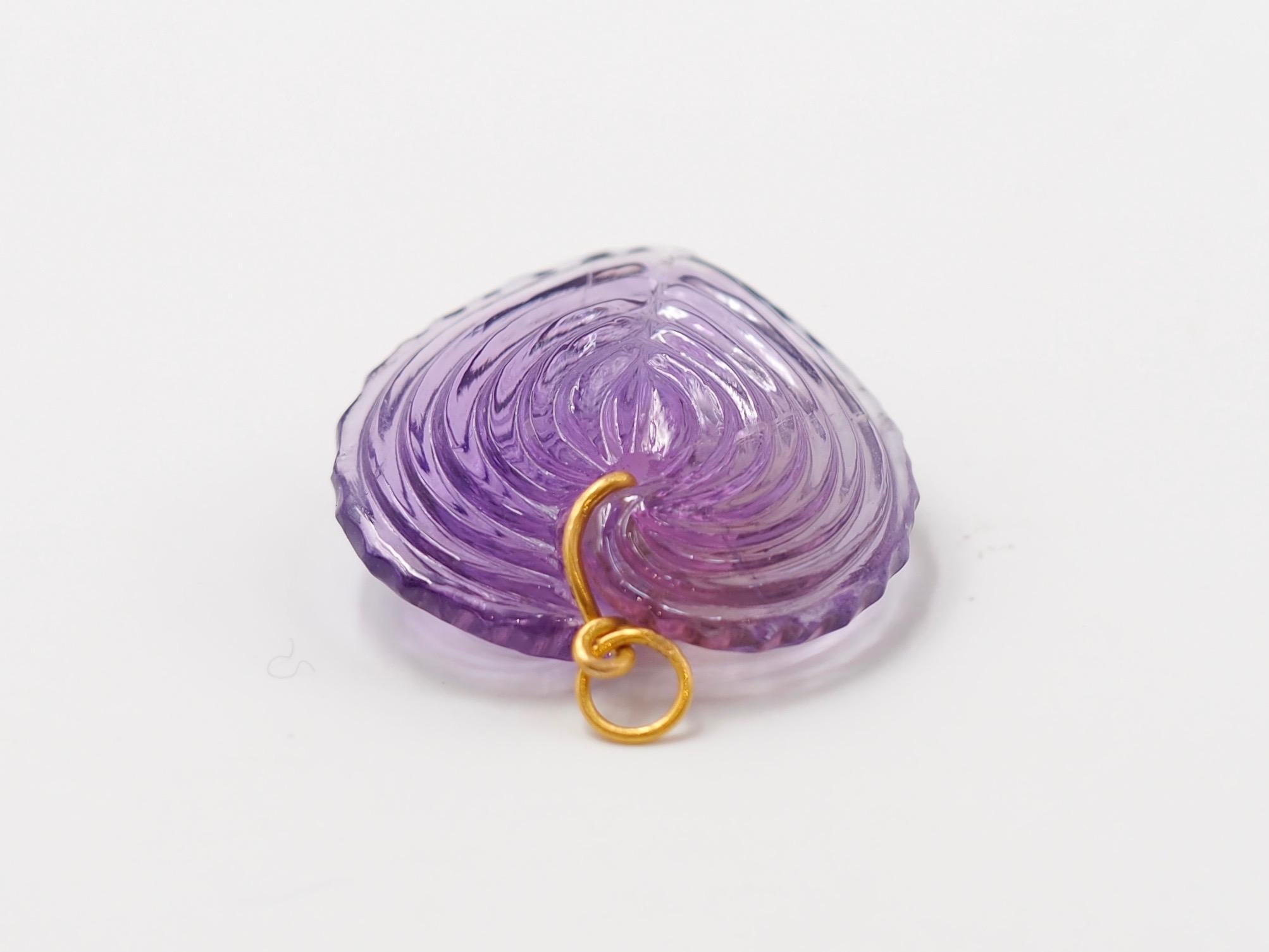 Hand-carved and handmade, this pendant represents a heart seashell in amethyst. The stone is simply drilled to allow a curved 22 karat gold wire that is twisted and finishes with a ring. 

2 sizes exist as you can see on one of the photo. This