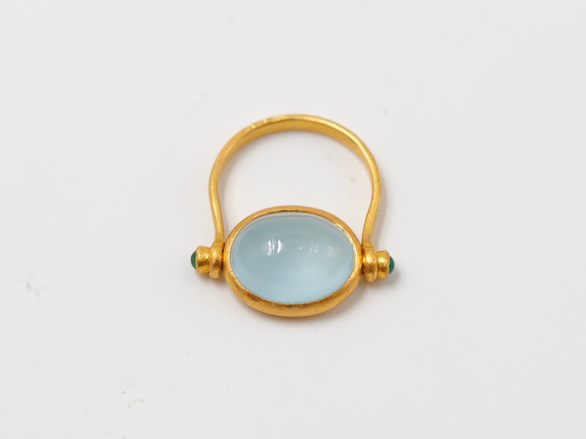 This antique style ring by Scrives is set with a luminous opaque aquamarine cabochon of 5.21 cts and 2 small emerald cabochons (0.15 cts) on the side of the aquamarine. 
The central stone and its setting are turning in order to give more comfort.