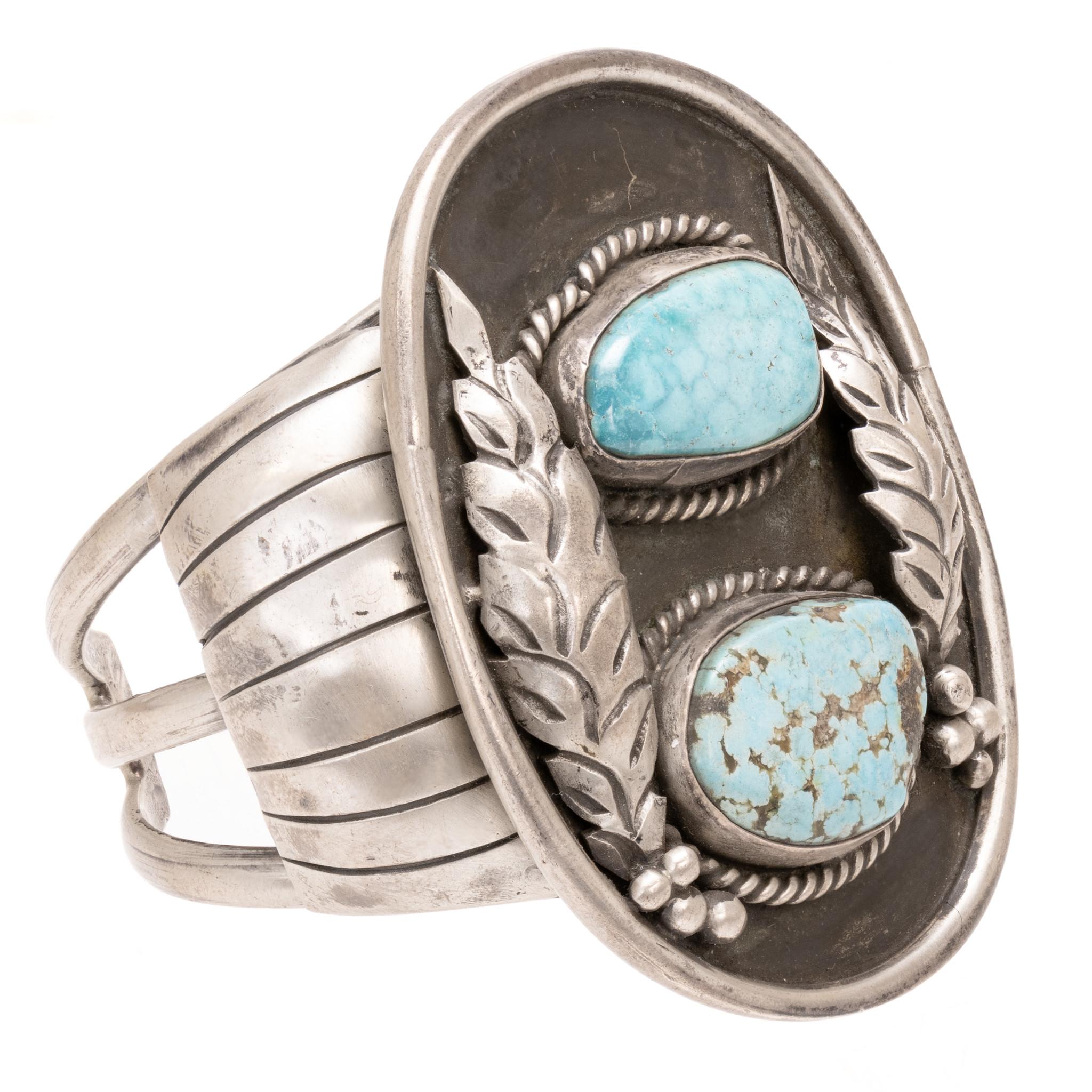 Bracelet manchette en turquoise et argent. Grand bracelet avec deux pierres serties dans une boîte d'ombre et entourées d'une bordure de corde torsadée, avec des plumes et des perles en argent de part et d'autre. Un épais motif en sterling hachuré