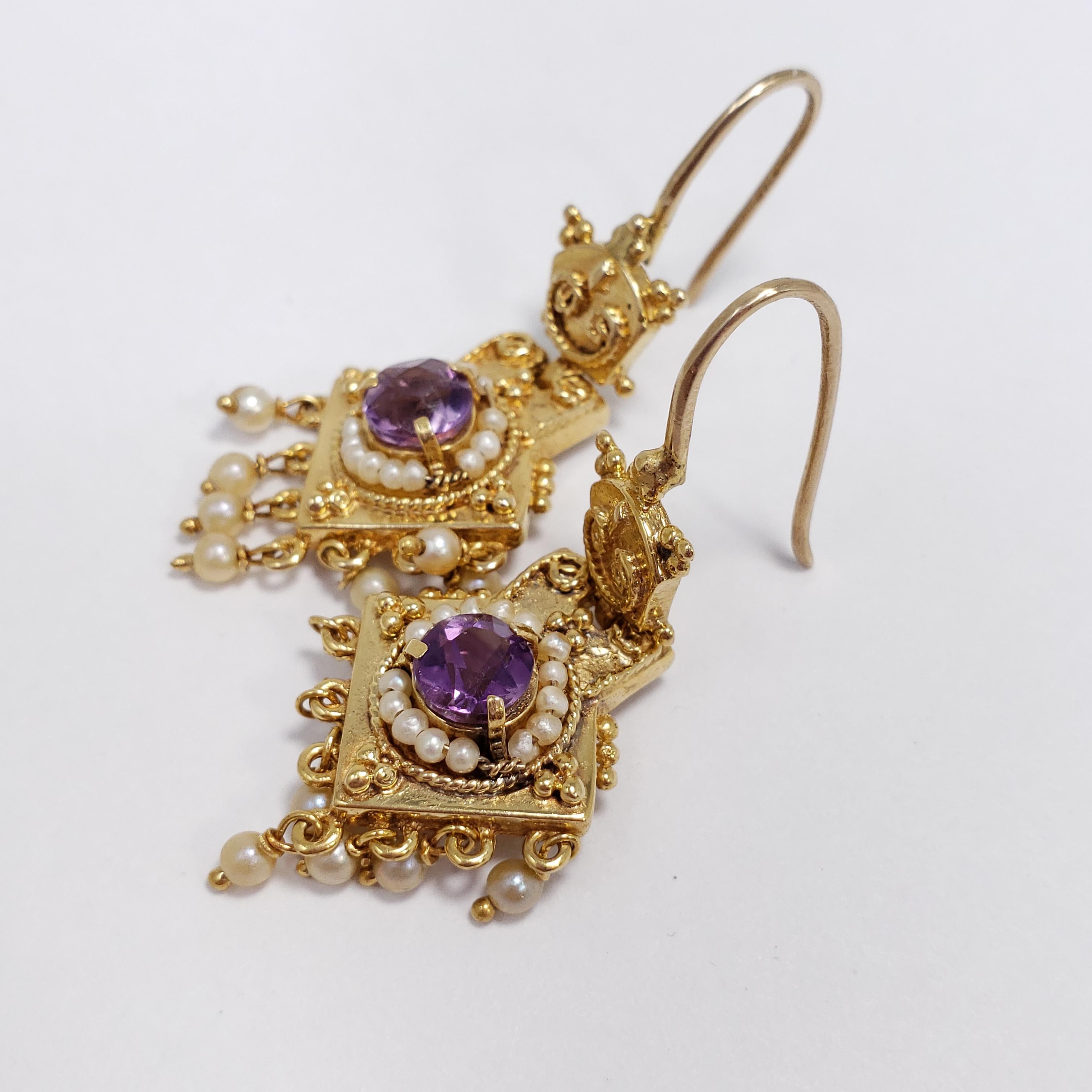 A stylish pair of Victorian earrings that radiate elegance! Each earring features a prong-set amethyst set in 14KT gold. Seeded pearls encircle the amethyst, and also hang off the bottom of the ear for a sophisticated touch. The earrings consist of
