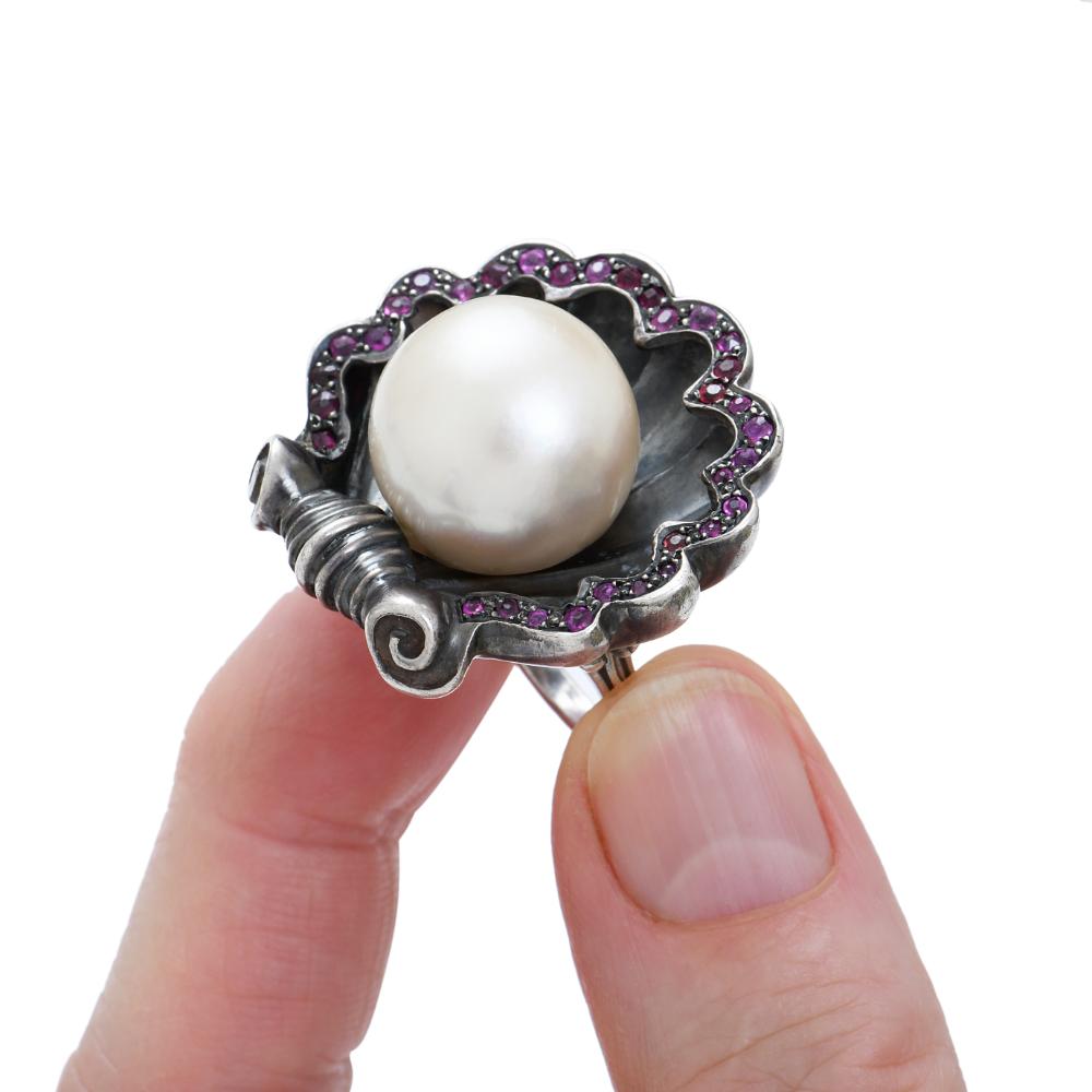 One of a kind shell shape ring in patinated  silver with a 3/4 of a south-sea pearl in the center by Sylvie Corbelin.
All around the shell border 2 carats of rubies.
The mount of the ring is in 925/1000 silver : 20 grams
Diameter of the south sea