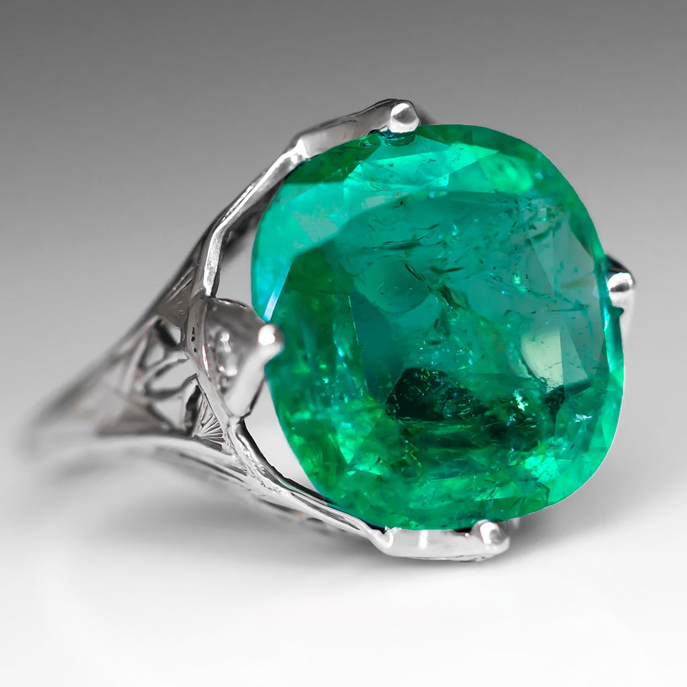This stunning 1930's emerald cocktail ring is centered with a 5.5 carat cushion cut emerald. The emerald is four prong set and each prong is accented with a single cut diamond. The shoulders and gallery of the ring are pierced filigree and are