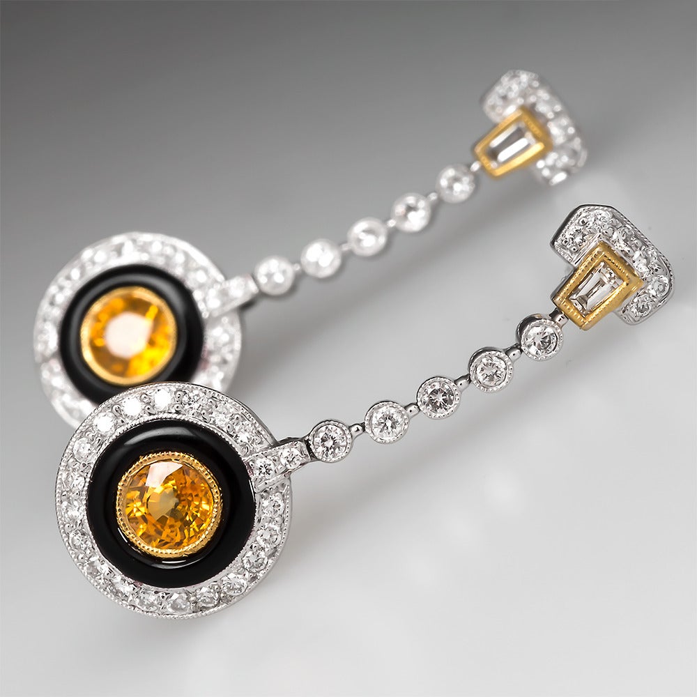 These gorgeous earrings are crafted of solid 18k two-tone gold and feature geometric drop sections set with diamonds, black onyx, and yellow sapphires. The top of each earring has a tapered baguette diamond bezel set into yellow gold finished with