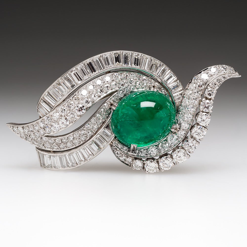 This beautiful vintage brooch is crafted in platinum and features a 16.79 carat oval emerald cabochon. It is also fitted with a bale to be worn as a pendant. The emerald is surrounded by a sea of 7.4 carats worth of very high quality sparkling