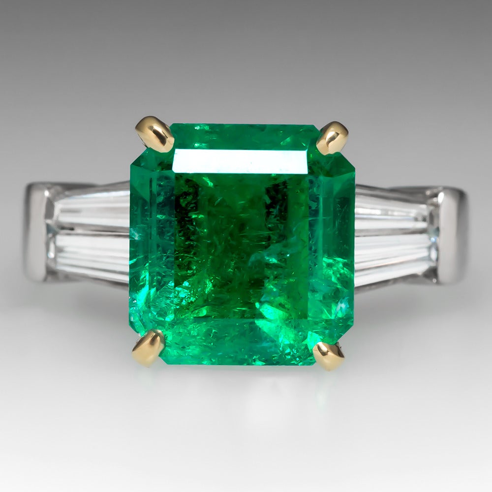This phenomenal natural emerald engagement ring features a stunning high quality center stone flanked by a full carat of tapered baguette diamonds. The ring is in very good condition and is crafted of solid platinum with an 18K yellow gold head. The
