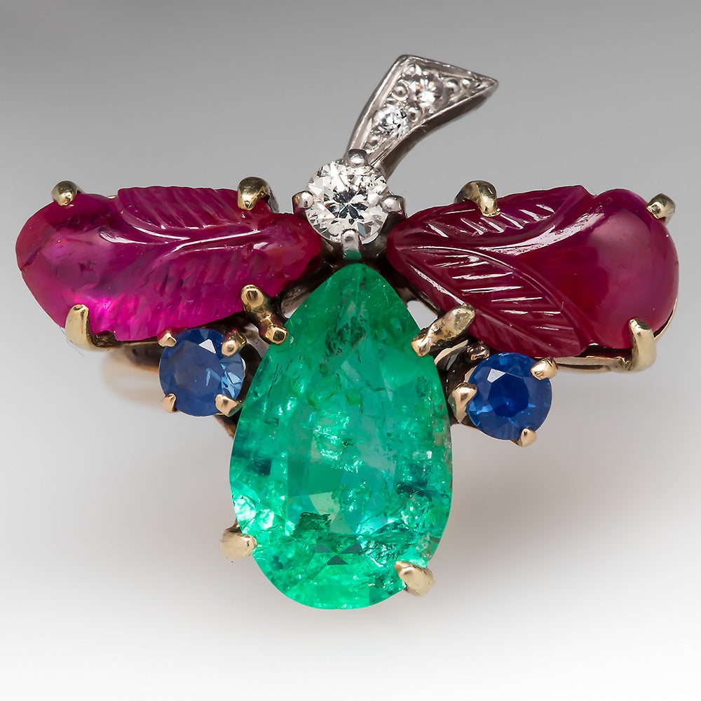 This incredible flower ring features a nice large emerald with blue sapphire and diamond accents, and intricately carved ruby cabochon leaves. This ring is crafted of solid 14k yellow gold and topped in platinum. It's in great shape. We left it's