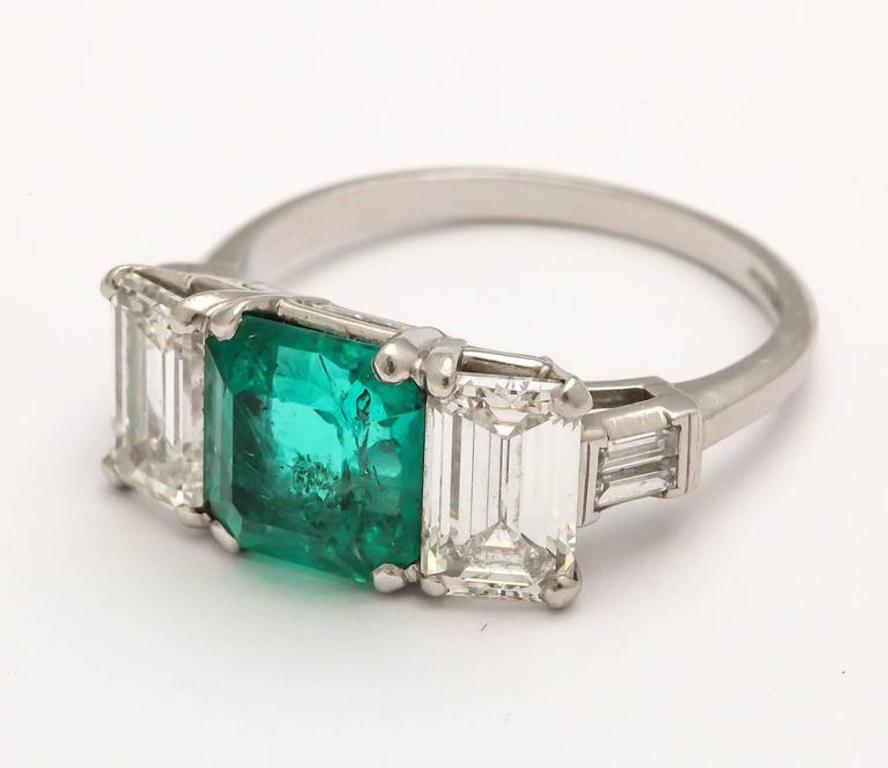 A stunning Art Deco ring with a vintage Colombian 2.50 carat medium tone strong saturation Emerald. Flanked by two Emerald 1-carat diamonds VVS/VS color G/H along with two smaller straight baguettes set in platinum. 
As with most emeralds there are
