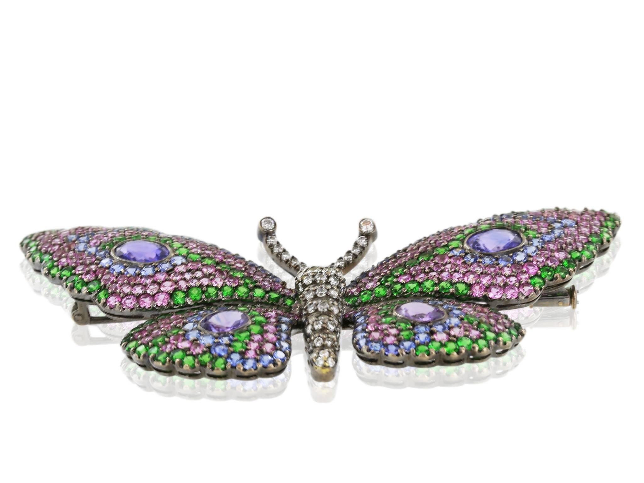18 karat white gold butterfly pin featuring 4 oval amethyst stones weighing approximately 2.40 carats surrounded by full cut round tsavorite and pink and blue sapphires on the wings and full cut diamonds on the body with an approximate weight of