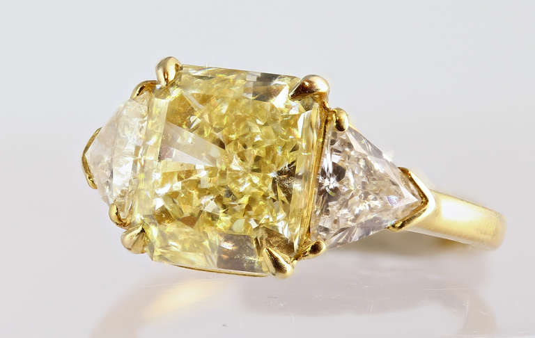 18 karat yellow gold Cartier ring consisting of one fancy yellow radiant cut diamond  having a total weight of 4.05 carats with a color/clarity of FY-VS1 respectively flanked by 2 white trillions. GIA 610719985121