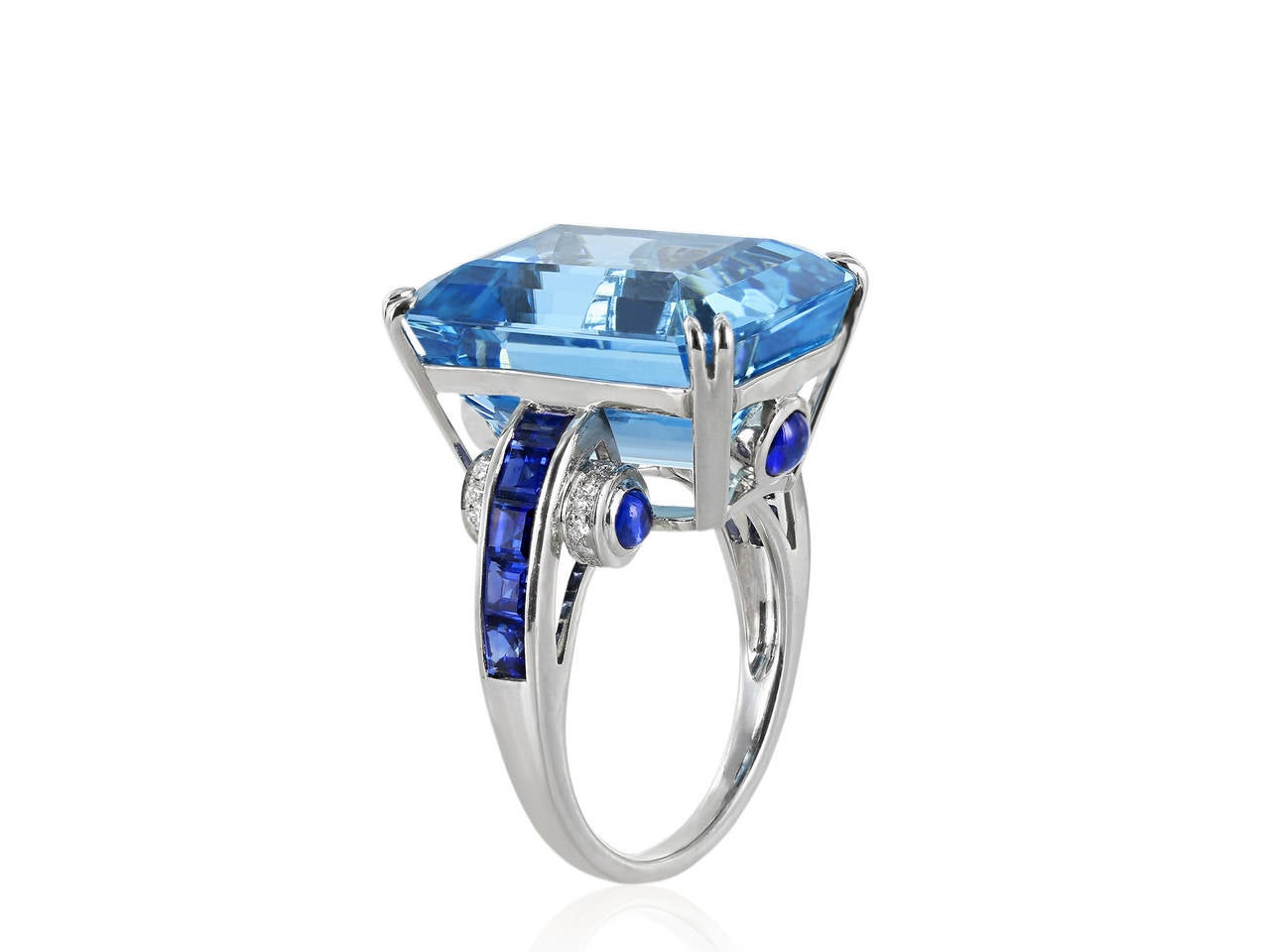 Estate platinum ring consisting of a 1 emerald cut aquamarine weighing approximately 18 carats flanked by 10 French cut sapphires with 6 cabochon cut sapphires accenting the under gallery and full cut diamonds.
