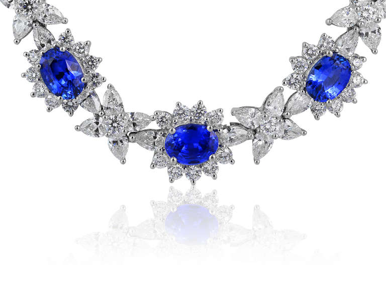 18 karat white gold cluster necklace set with approximately 15 carats of oval shaped blue sapphires and approximately 27 carats of full cut and fancy shaped diamonds having a color and clarity of F/VS1.