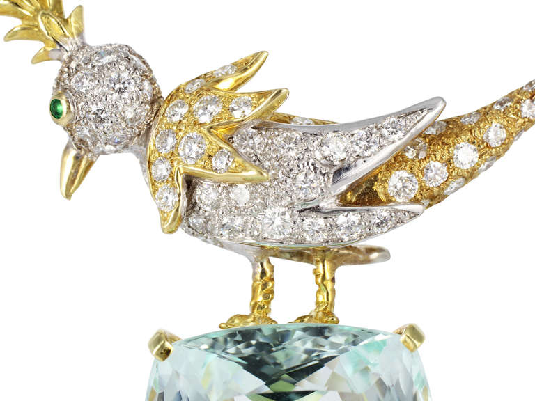 Two tone 18 karat yellow and white gold estate pin. Bird on a Rock brooch, consisting of 1 cushion cut aquamarine weighing approximately 52.92, the stone set with a full cut diamond encrusted bird with faceted emerald eye.