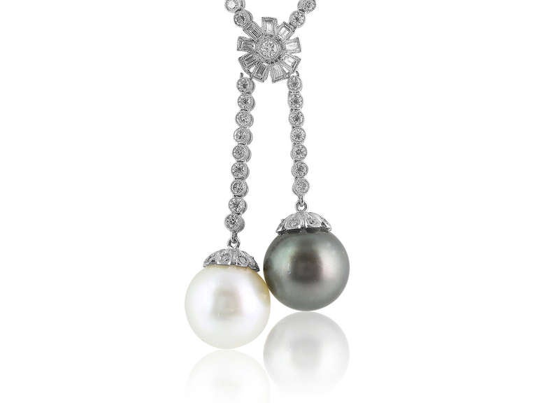 18 karat white gold 20 inch drop necklace consisting of 6.45 carats of round cut diamonds  that are milgrain bezel set with a baguette flower shape connector at approximately 16 inches with 1 black 14.29MM South Sea pearl and 1 white 14.32MM South