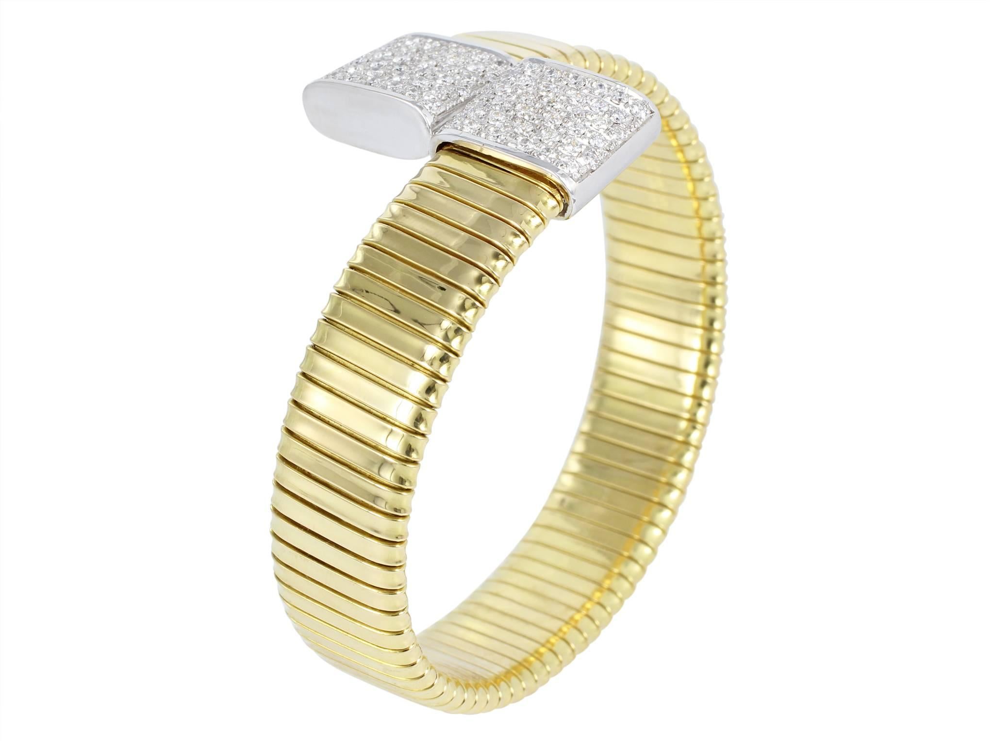 18 karat two tone yellow and white gold flexible flat coil style bypass cuff bracelet consisting of 2 end caps accented with pave set full cut diamonds having a total weight of 1.15 carats.
