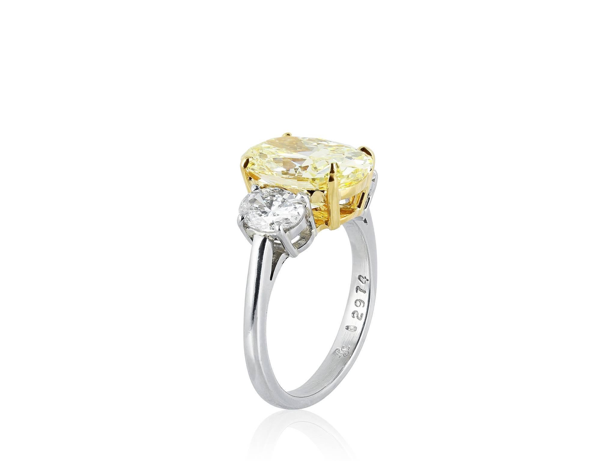 Platinum and 18 karat yellow gold custom made 3 stone ring consisting of 1 oval brilliant natural fancy yellow diamond weighing 4.55 carats having a color and clarity of FY/VS2, measuring 12.97 x 9.10 x 5.83 mm, with GIA certificate #15062114, the