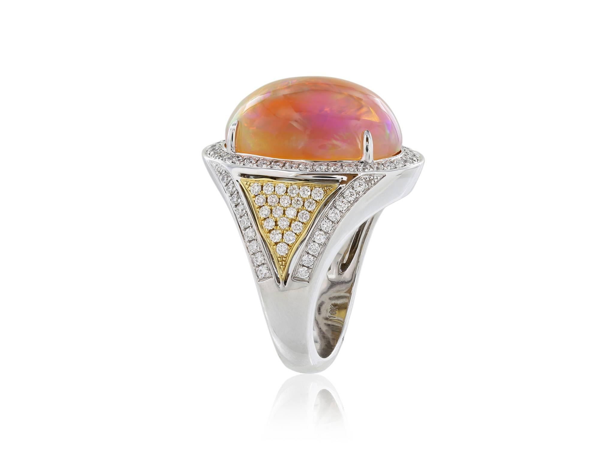 18 karat two-tone white and yellow gold ring featuring  1 cabochon orange opal weighing 12.36 carats. The oval opal is surrounded by pave set diamonds. The shoulders have a YG triangle bezel filled with pave set diamonds and white gold shank is also