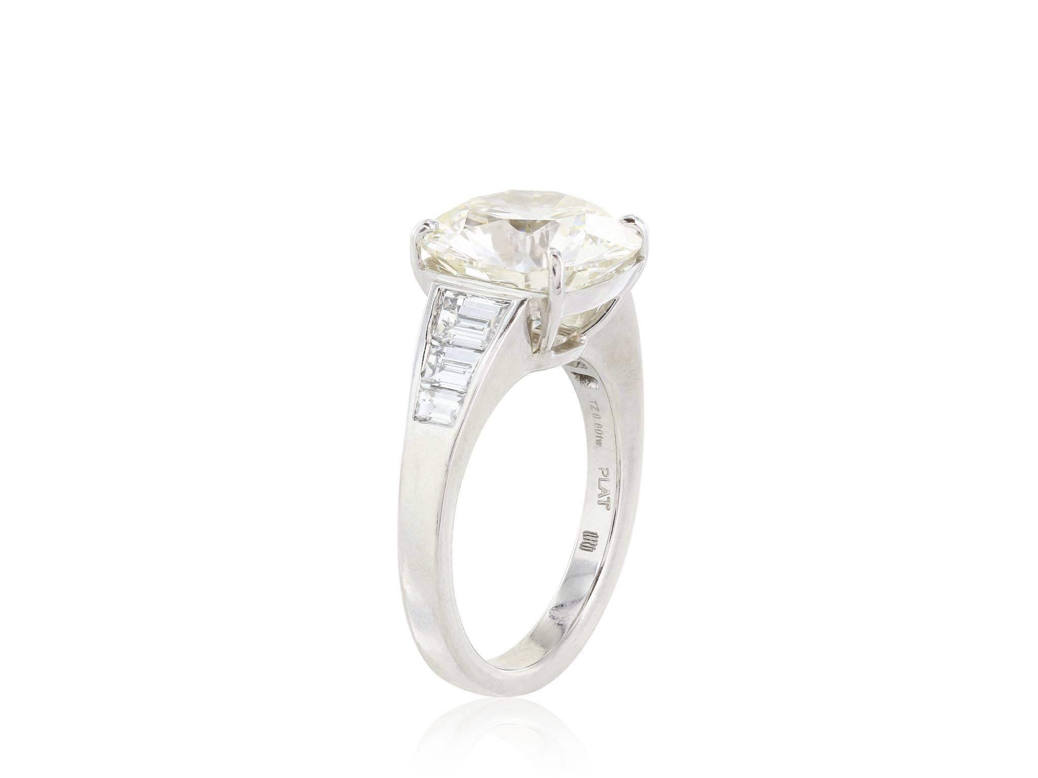 Platinum set diamond ring, featuring one GIA certified 5.60 carat round brilliant cut diamond having a color and clarity of J/SI1 (GIA cert#5151786069). The diamond is flanked by six trapezoid cut diamonds with a combined weight of .80 carats, a