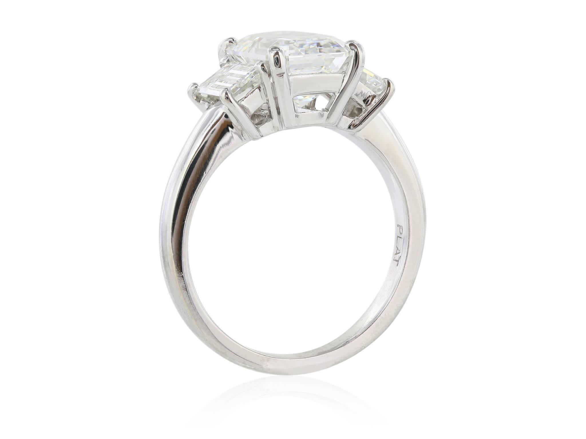 Platinum set custom made three stone diamond ring featuring one GIA certified emerald cut center stone weighing 3.01 carats with a color of G and a clarity of VS2.  The center diamond is flanked by two emerald cut sides stones, each with a color of