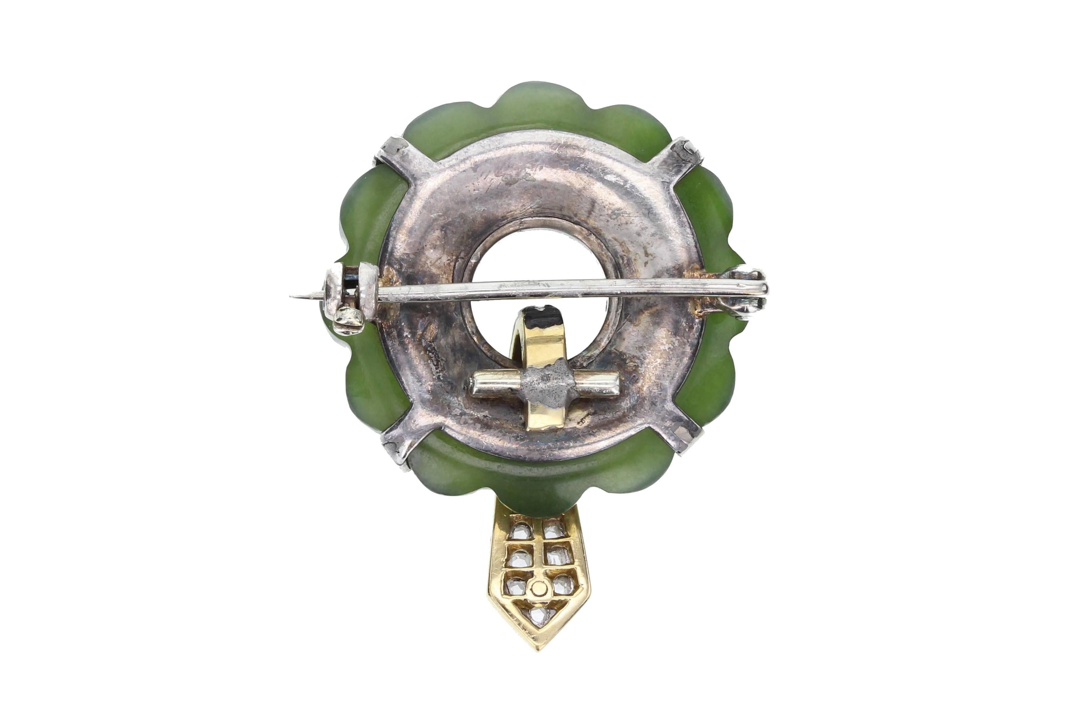 Deep green carved jade piece with a pierced centre mounted in four platinum claws, each set with a single rose-cut diamond. Black enamel detailing at the centre with a tapering gold-piece extending from the centre with black enamel border and pave