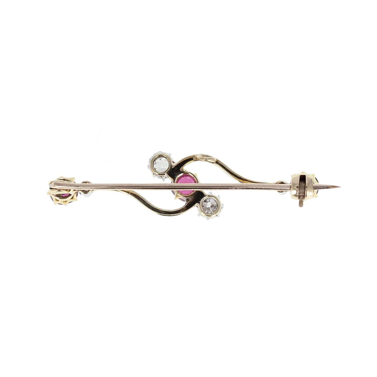 A classic bar brooch in 18 carat gold featuring a central trio of two old-cut diamonds and a ruby set on a twist, with a further ruby and diamond set at each end. Elegant and simple with fine quality gemstones.
Specifications:
 
Setting
Tests as 18