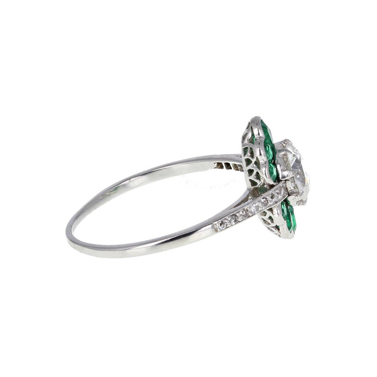 In outstanding condition and of excellent quality, this platinum ring features a central transition-cut diamond exhibiting exceptional brilliance. Topped and tailed with a fan of calibre-cut emeralds to give a oval shape. Single-cut diamonds set in
