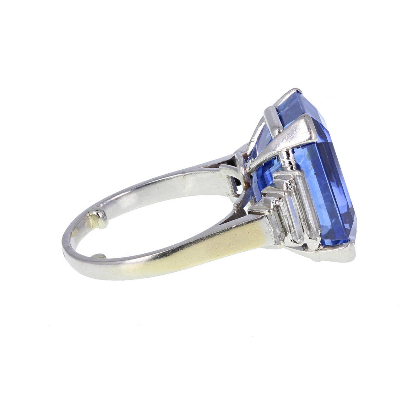 An exquisite and rampant Art Deco ring featuring and emerald-cut Ceylon sapphire, flanked by stepped baguette cut diamonds on each side. Mounted in platinum and 18 carat white gold and accompanied by an SSEF certificate stating that the sapphire has