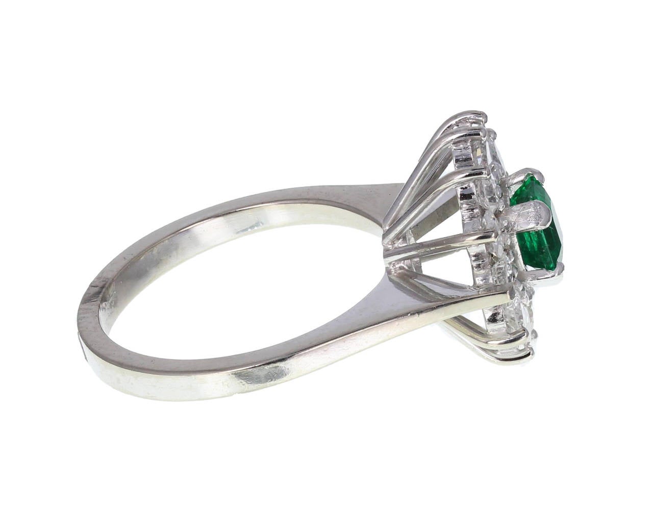 Central emerald-cut emerald of exquisite deep green colour, mounted in four claws, surrounded by 12 round, brilliant-cut diamonds, each in two claws. A beautiful quality cluster ring. Approximately 0.60 of a carat of emerald. Approximately 1.20