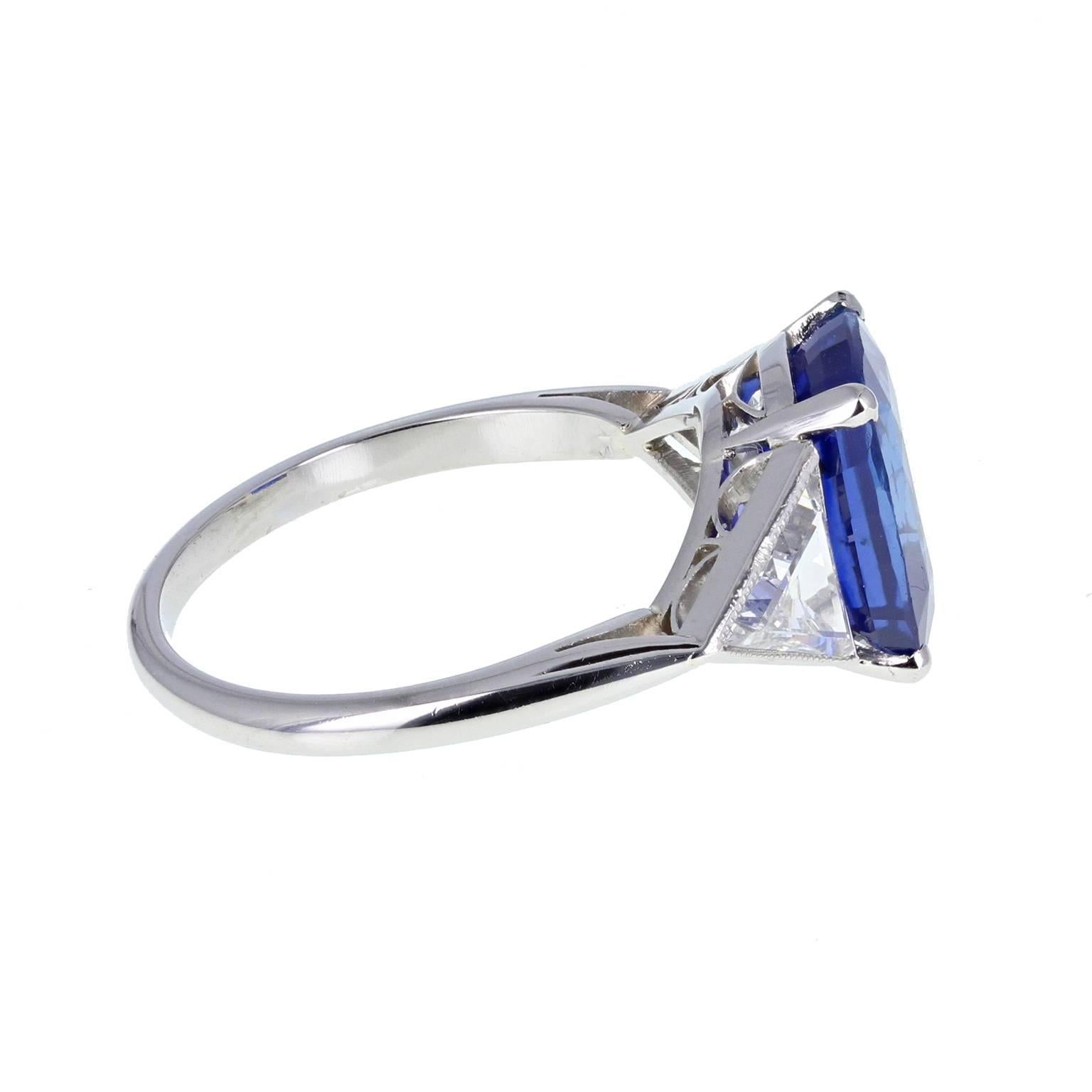 An exceptional Ceylon cushion-cut sapphire weighing 5.00 carats is mounted in four claws and accented on each side by a single trillon-cut diamond in millegrain edged rubover settings. An outstanding sapphire that exhibits the coveted royal blue