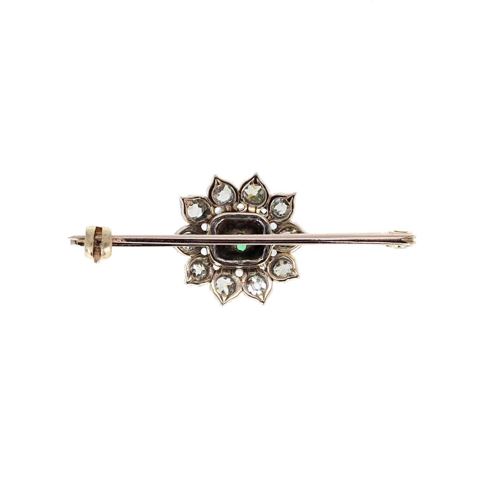 This antique pin brooch is set with a central cluster. A square-cut emerald of exceptional colour is mounted in a bezel setting, surrounded by ten 'petals', each set with a single old mine-cut diamond. Some wear consistent with the age of the brooch