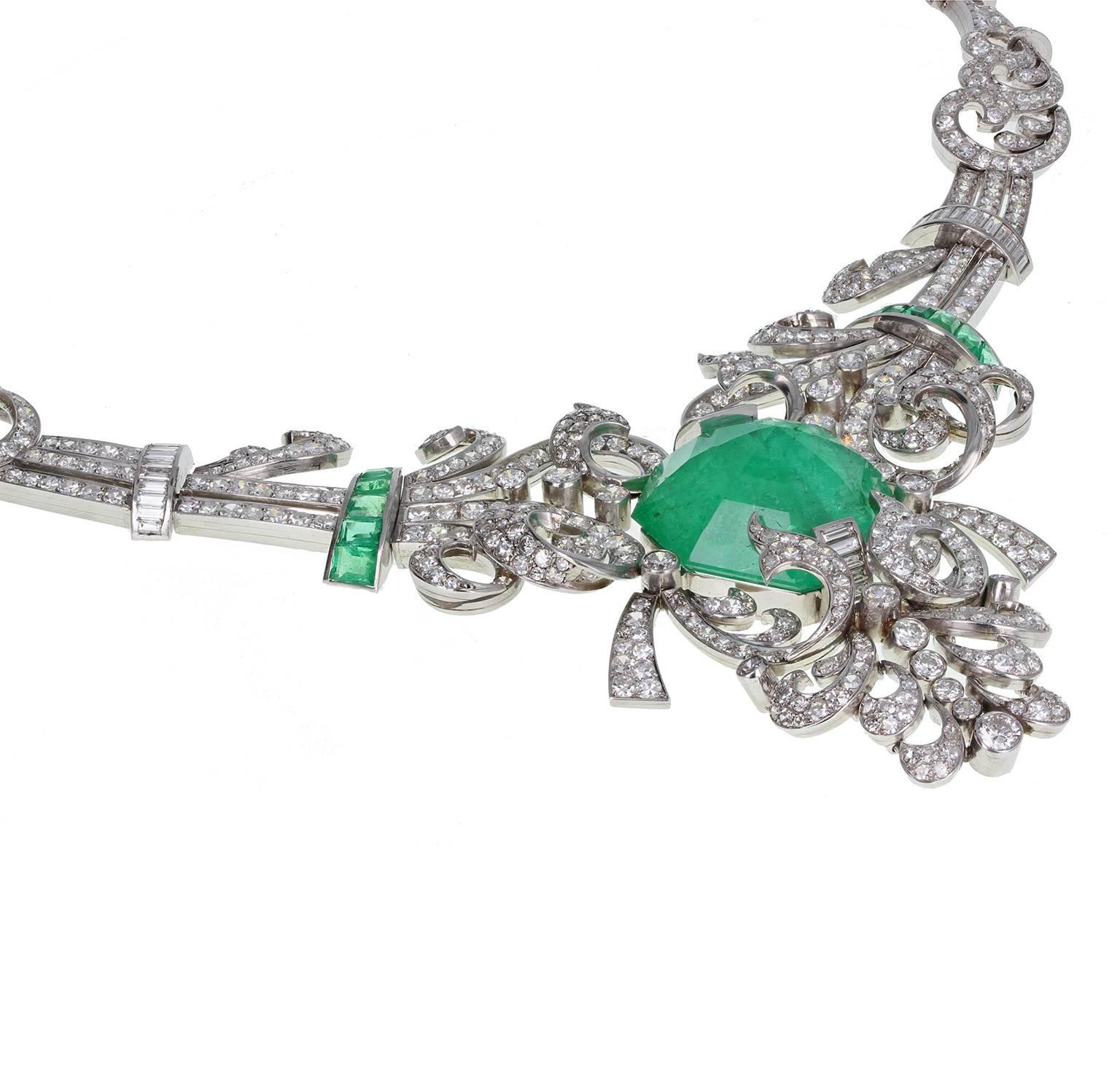 An exquisite French 1920s necklace in platinum. A dramatic and impressive necklace comprising of swirls and swags of platinum, set with single-cut and brilliant-cut diamonds, centred around a single, massive octagonal-cut Colombian emerald of