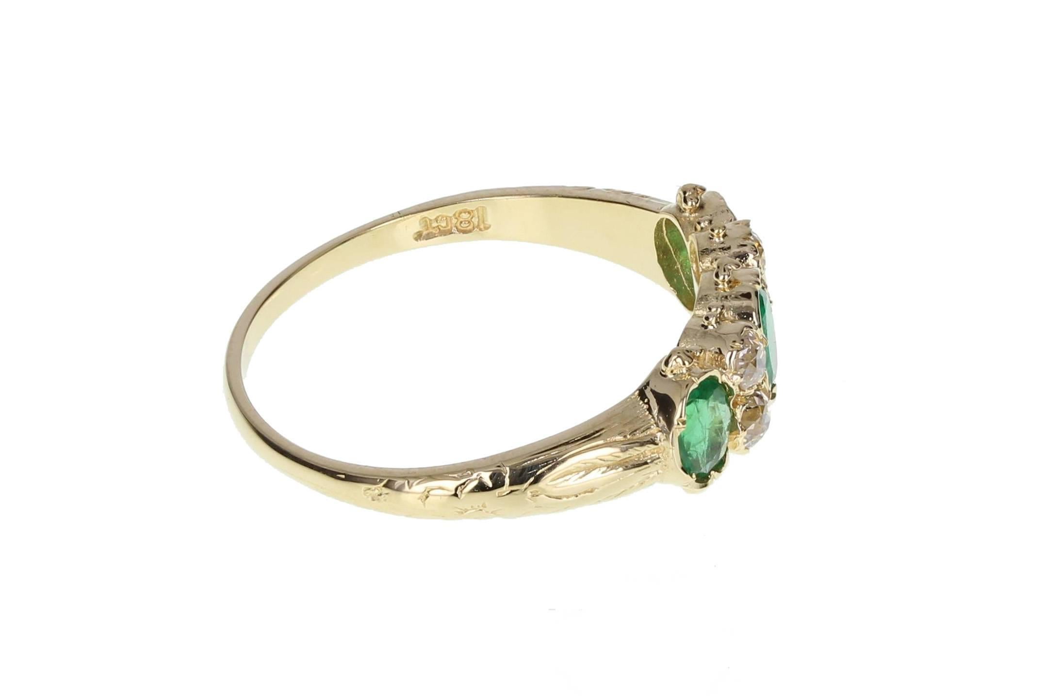 This very fine antique ring in 18ct gold features three exceptional quality emeralds of deep, well saturated green colour and good clarity, accented by particularly bright and lively old-cut diamonds. Carved scroll-work to the shoulders and a