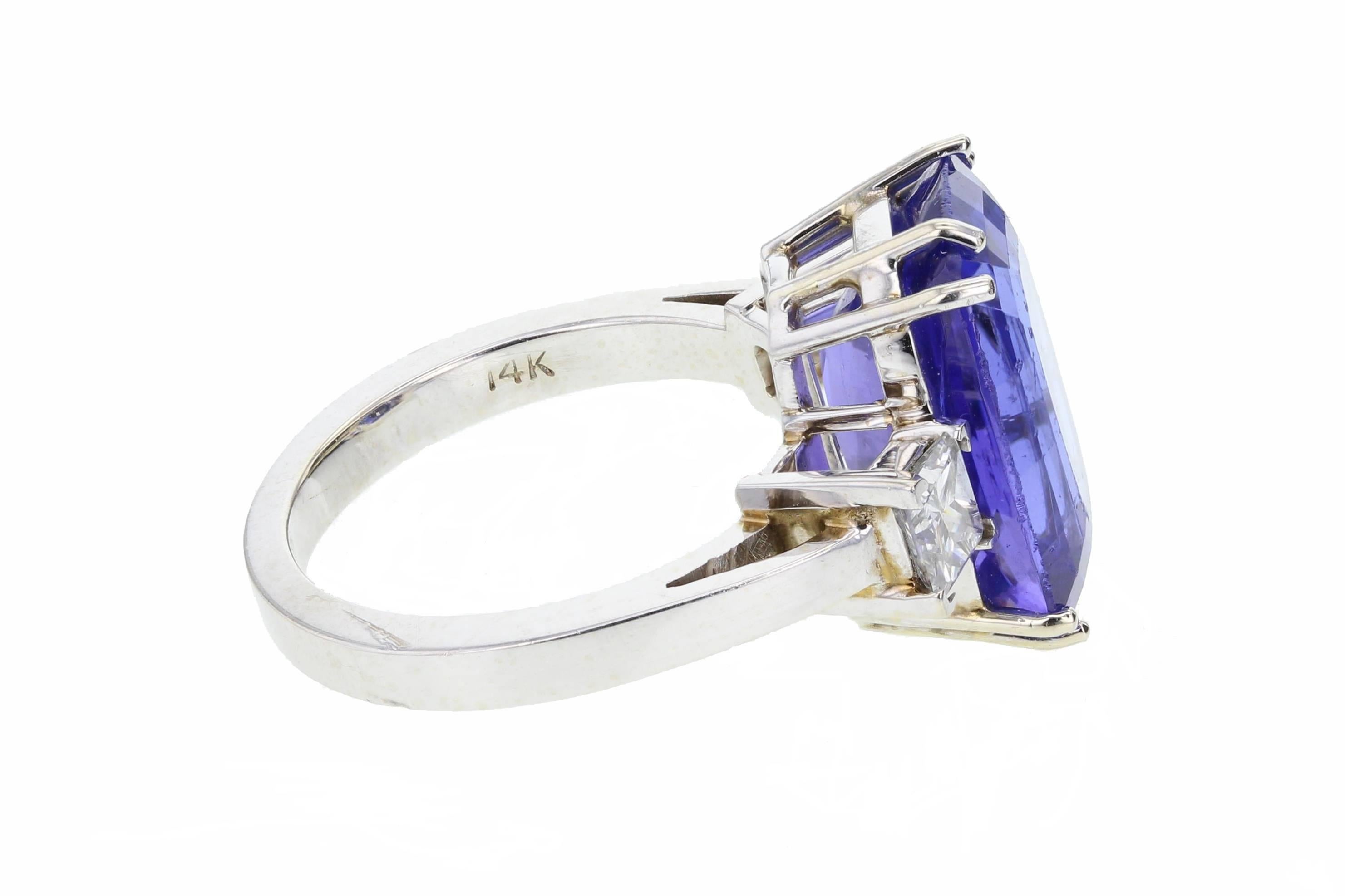 This wonderful ring is set with a large squared-oval tanzanite of top quality, exhibiting the unmistakable purple/blue. Flanked on each side by a single princess-cut diamond. A plain, squared shank. A very fine example of beautiful tanzanite.
