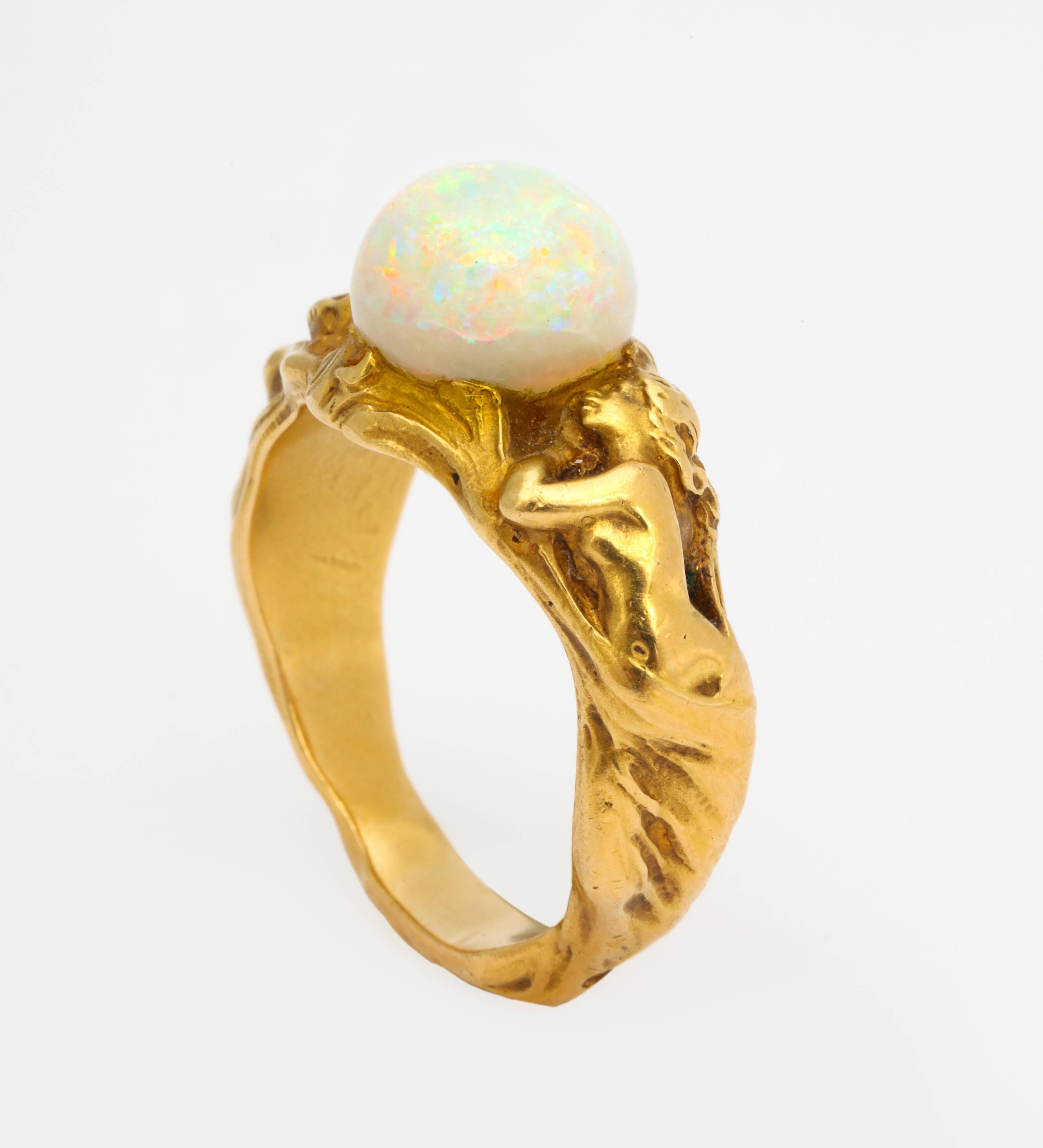 A large scale 18K gold Art Nouveau ring, of beautifully sculpted draped nudes revealing themselves, and crowned by a lively 10 mm opal, suited for man or woman size 9 1/2. Unmarked.