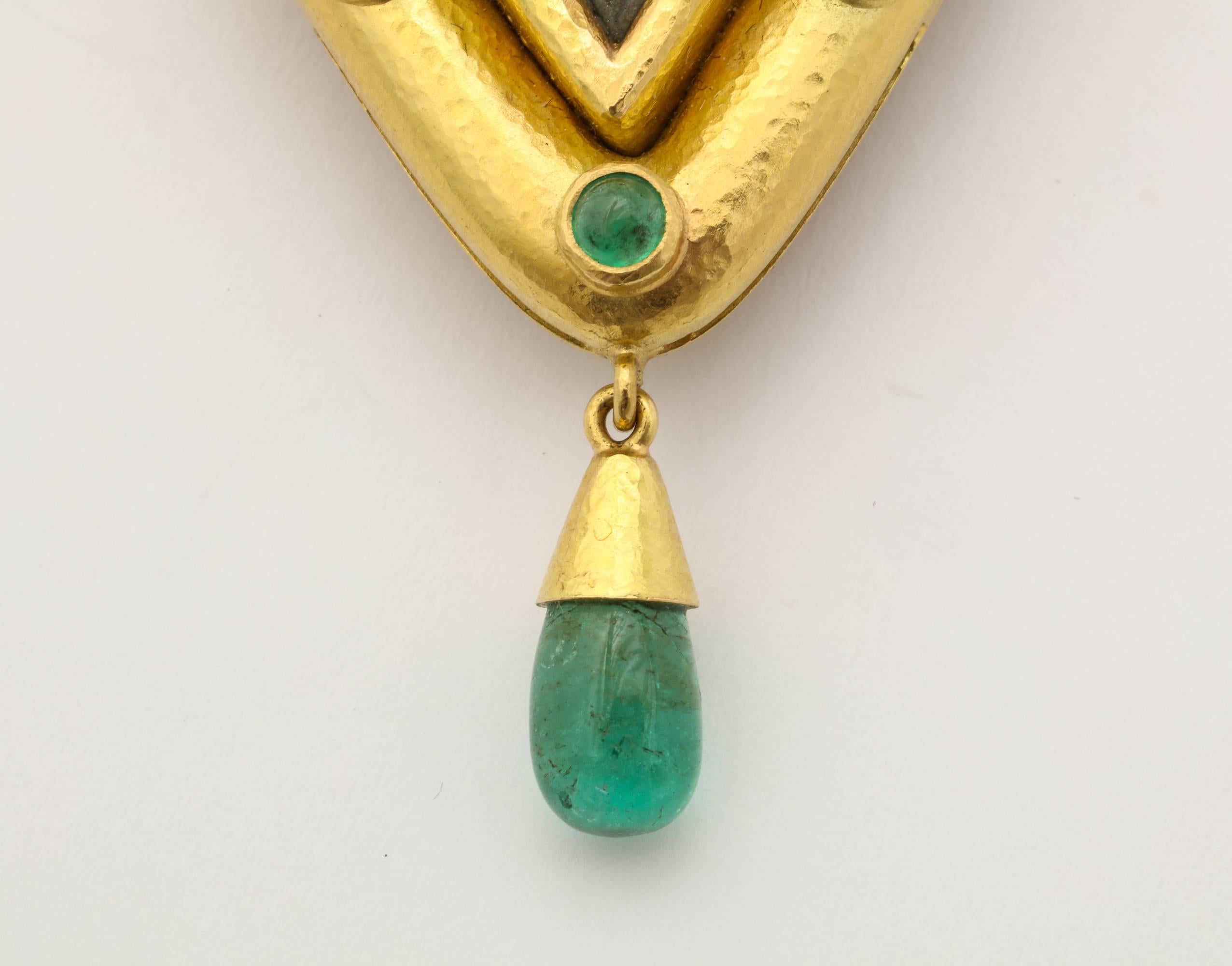 A beautifully crafted combination pendant/brooch by Elizabeth Locke of textured 18K gold, framing an antique lava carving, and set with cabochon emeralds and hung with an emerald drop. The bale is removable and the ring folds away for a clean edged