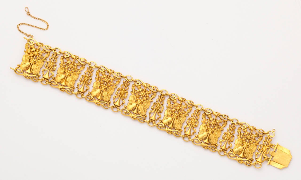 From the turn of the century comes a delicate and beautifully made Continental 18K gold bracelet of scrolling edged links alternating between narrow segments as ribbon tied trumpets, and wider openwork links featuring violins and cellos, their bows,