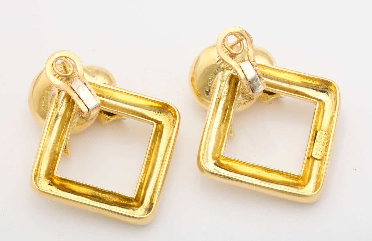 Stylish 1980s ear clips made in Italy for Cartier, as a tubular square form hung from one corner generously tied as a large knot. Clip backs with a post, easily worn from day into night. Cartier mark, gold mark, and registry numbers. 1 5/8 inches x