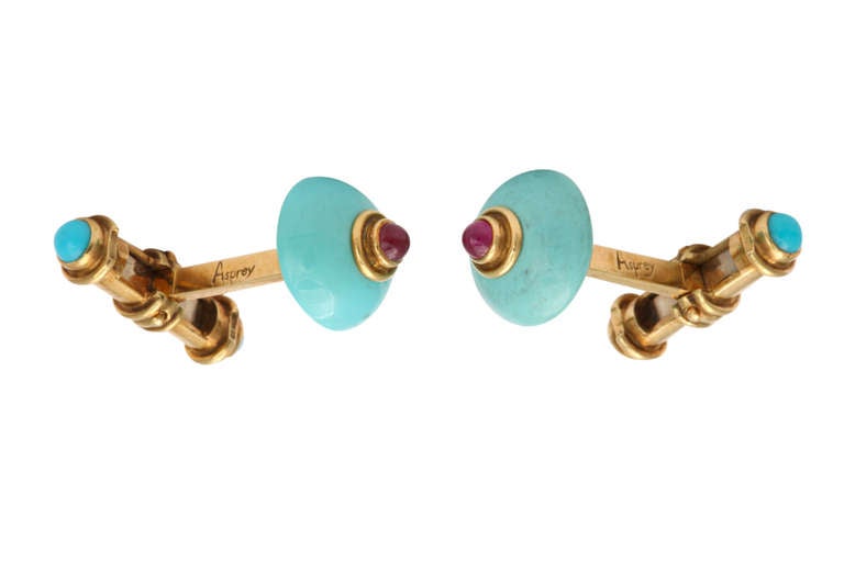 A handsome pair of Asprey cufflinks, in 18K gold featuring carved turquoise set  with cabochon rubies. The back bars, capped with cabochon turquoise, are hinged for eay installation. The main stone is 1/2 inch in diameter. Asprey and gold marks on