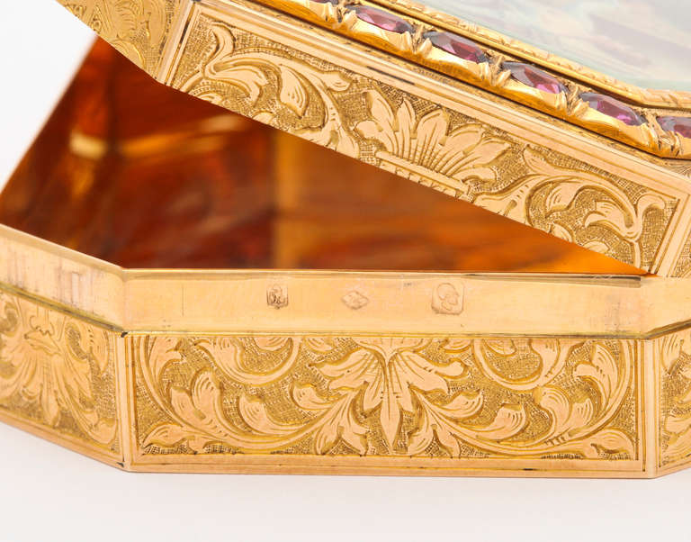 A luxurious 18K gold box, engraved overall with leafy flourishes and grape clusters, the back and corners with masks, the top holds a miniature painting under beveled glass depicting three figures in a garden setting, framed in gold set with 36
