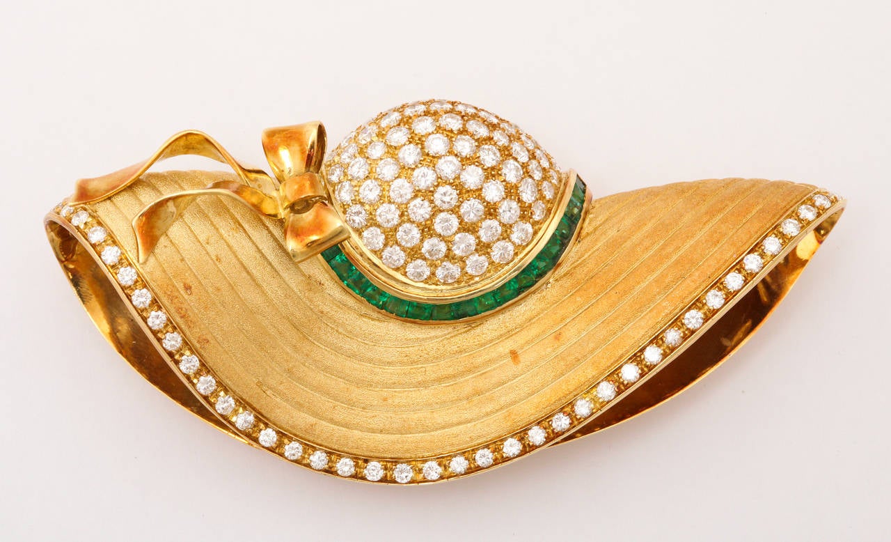 A charming and beautifully sculpted brooch and ear clip suite as 3 dimensional garden hats made of 18K gold, in a hand textured finish with the look of finely woven straw, the crown pave set with diamonds, a ribbon of calibrated emeralds, and the