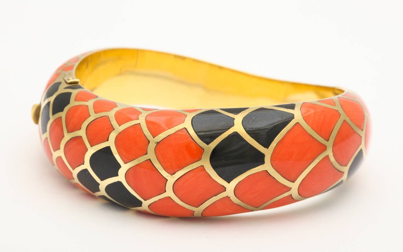 An exquisite Angela Cummings 18K gold bracelet of serpentine form inlaid with hand cut natural red-orange and black coral to resemble snakeskin. 1/2 inch at most narrow, and 3/4 inch at its widest. Fits a 6 1/2 inch wrist. 69.8 grams. Gold and