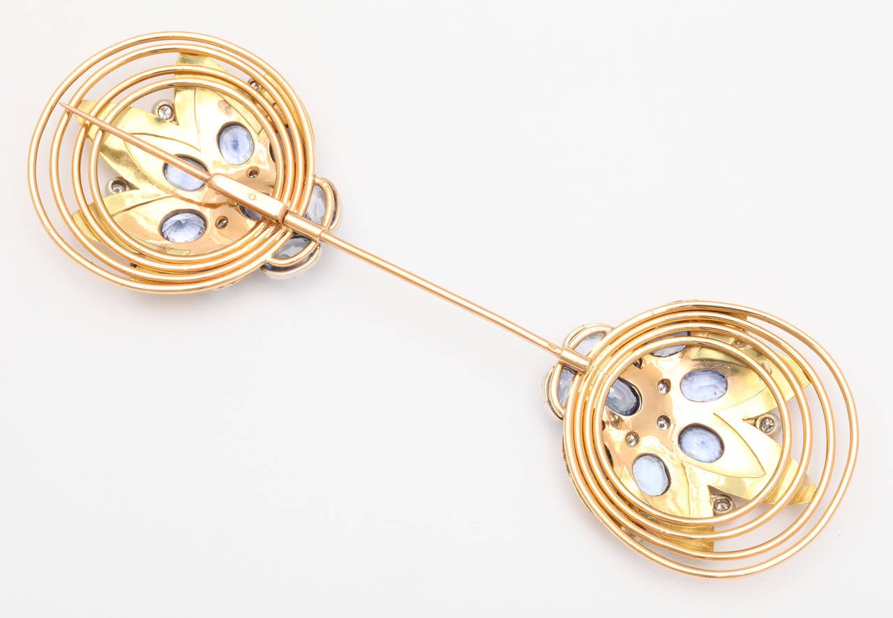 A beautiful Retro style French jabot pin made in three colors of 18K gold, featuring stylized flower blossoms highlighted against radiating hoops of gold, set with 16 cornflower blue sapphires and 18 accent diamonds. 18K Eagle stamp on pin, 750 mark