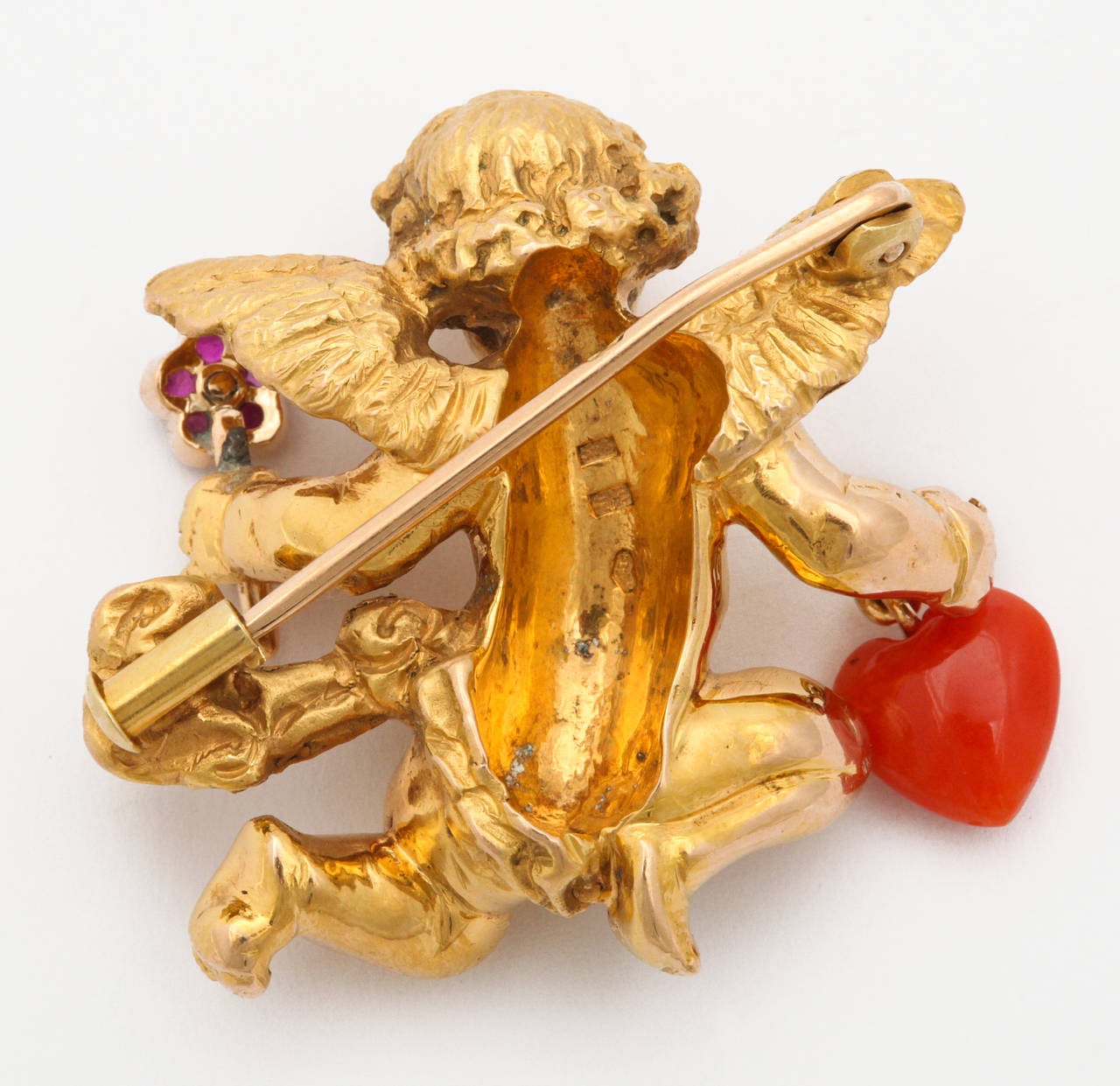 A charming and elegant figural brooch by the renown Viennese firm of Paltscho. A fine 18K gold representation of a cherub in flight, offering a ruby and diamond set flower in one hand, and a natural red coral heart in the other. Inspired by a