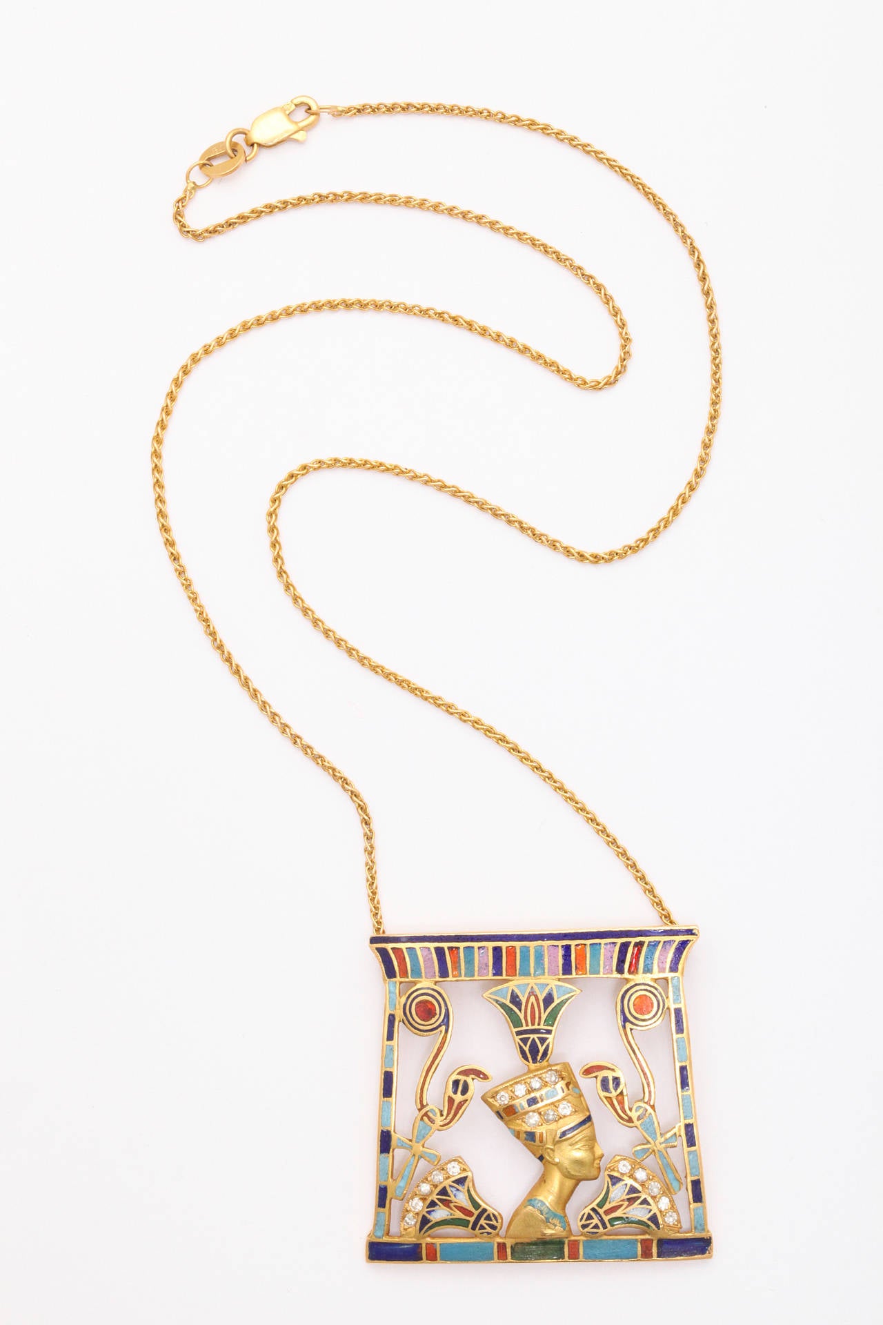 A striking pendant of Egyptian themes in18K yellow gold, featuring Queen Nefertiti, surrounded by cobra, lotus flower and Ankh (eternal life) symbols, set with diamonds and highlighted with multi color enamels. Unknown maker marks.  1 1/4 inches x 1
