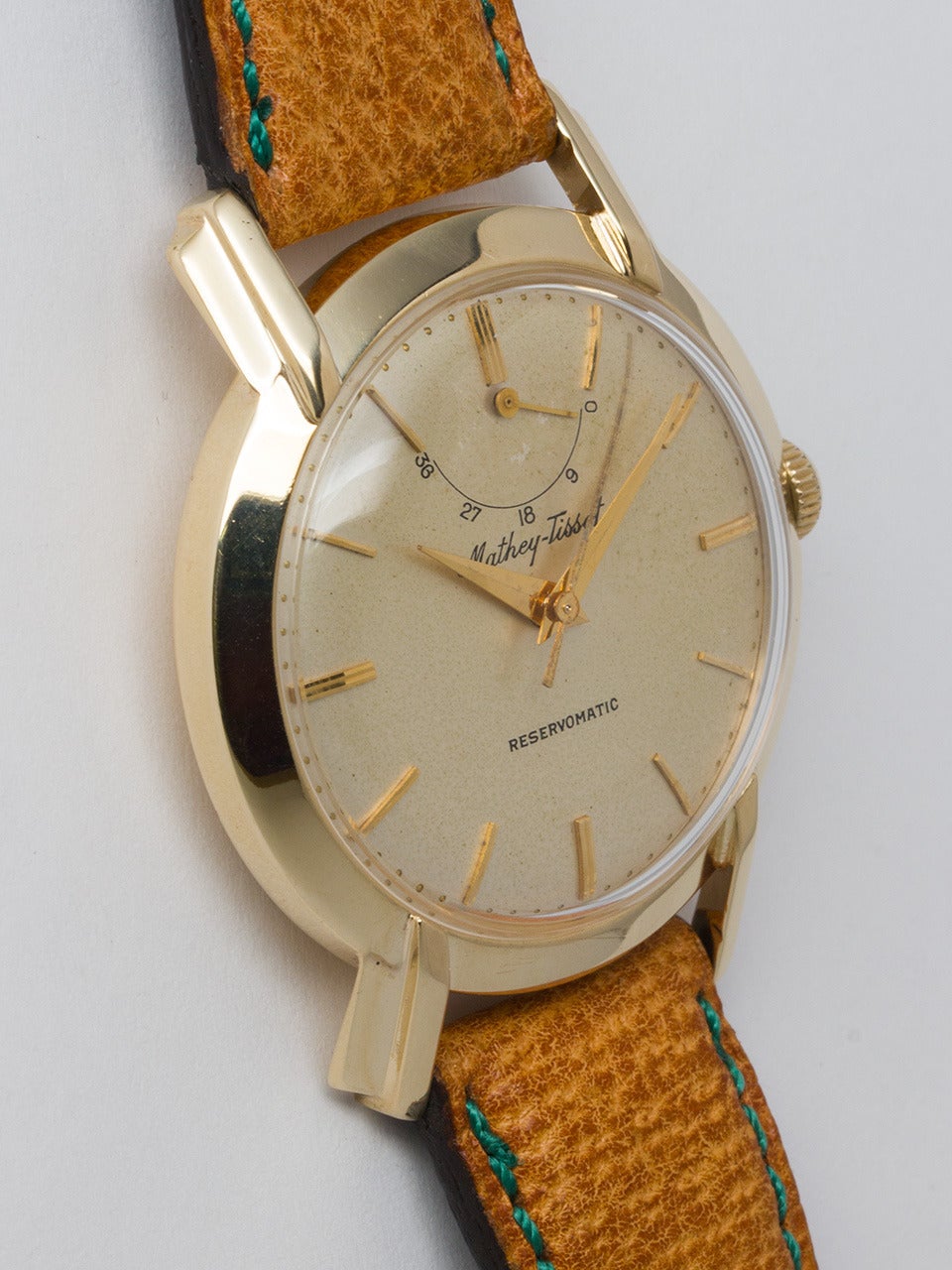 Mathey Tissot 14K Yellow Gold Reservomatic Wristwatch circa 1950s. 35mm diameter case with prominent fluted lugs. Very pleasing original cream dial with gold raised indexes and tapered sword hands. Self winding calibre 1282N movement with sweep