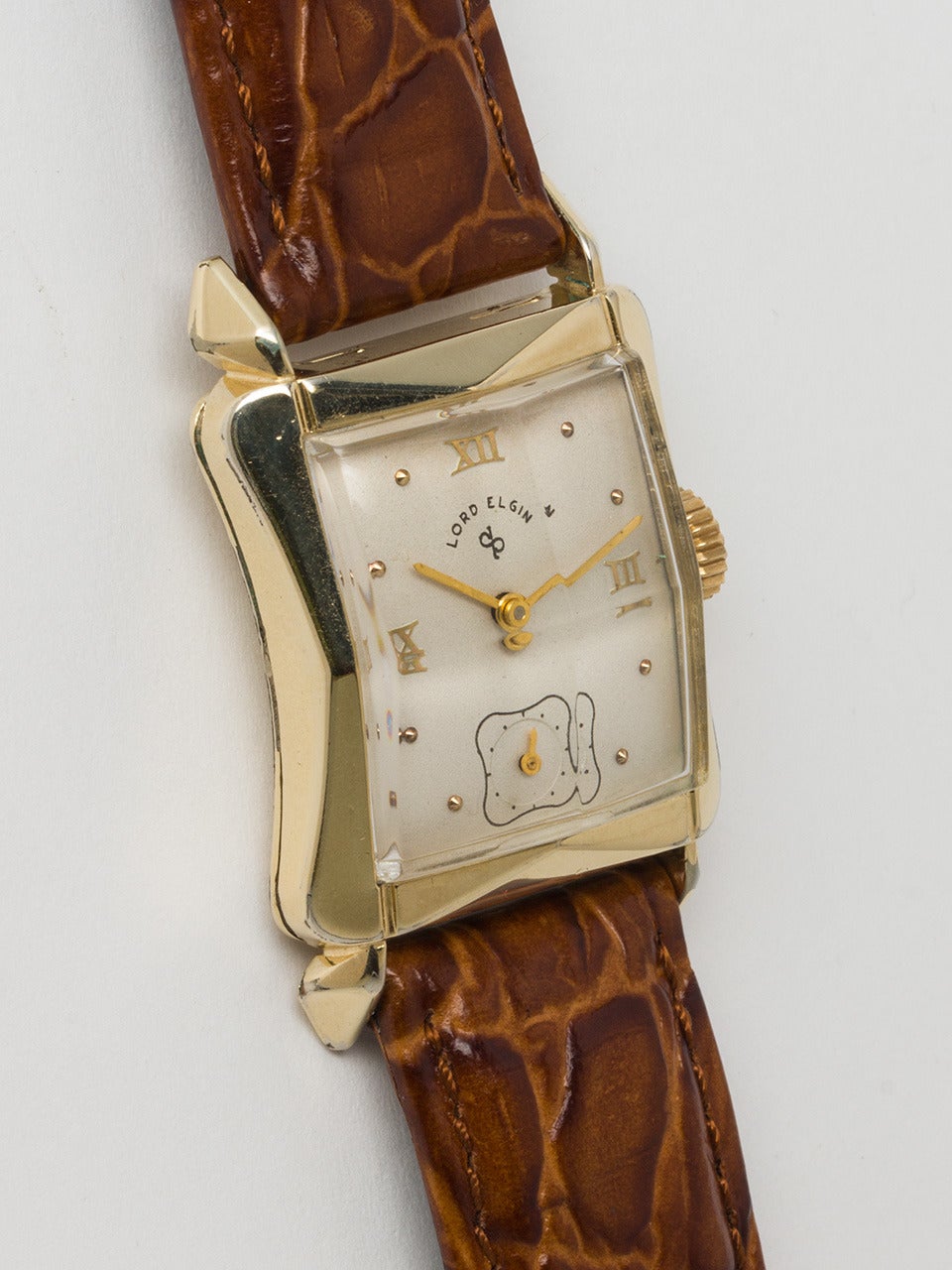 Lord Elgin Yellow Gold Filled Dress Model Wristwatch circa 1950s. Hour glass shaped case measuring 25x38mm with horn lugs and faceted rectangular crystal. With satin silvered dial with raised yellow gold Roman and dot markers. Powered by Elgin 670