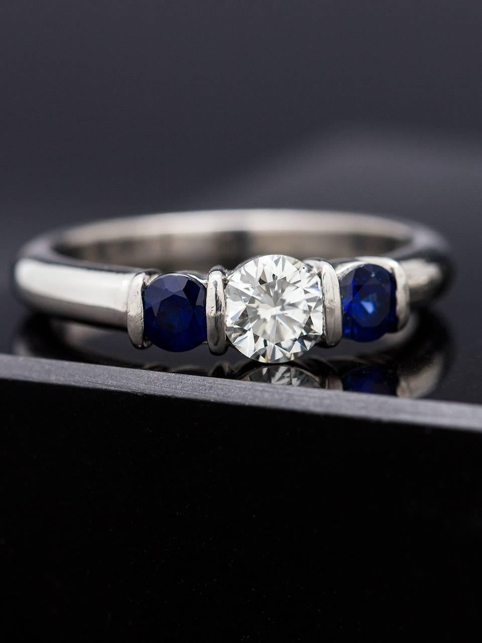 Simple, understated and versatile platinum three stone ring manufactured by Kwiat. The 5mm center round brilliant cut diamond weighs approximately 0.50ct, G/VS2, and is flanked by two bar set 3.5mm rich blue round sapphire side stones. Makes a