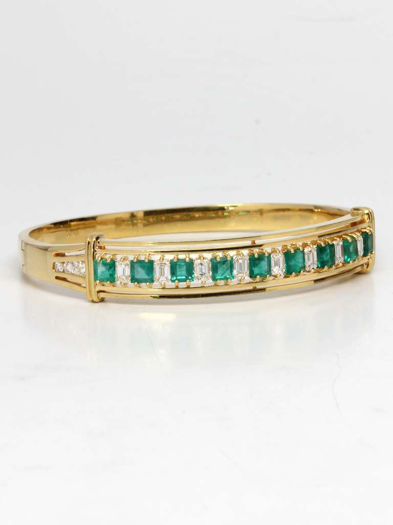 Gorgeous emerald diamond bangle hinged bracelet set in 18K yellow gold featuring 8 clean, white, sparkling emerald cut diamonds alternating with 9 square cut, bright green emeralds. There are 3 graduating size diamonds on either side.  Approximately