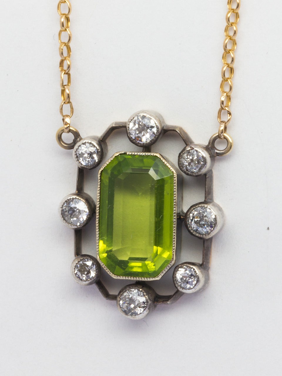 Hand made silver over gold setting with 8 bezel set Old European Cut diamonds approximately 0.80 carat total surrounding a beautiful green peridot, measuring 8mm x 13mm emerald cut. On 16