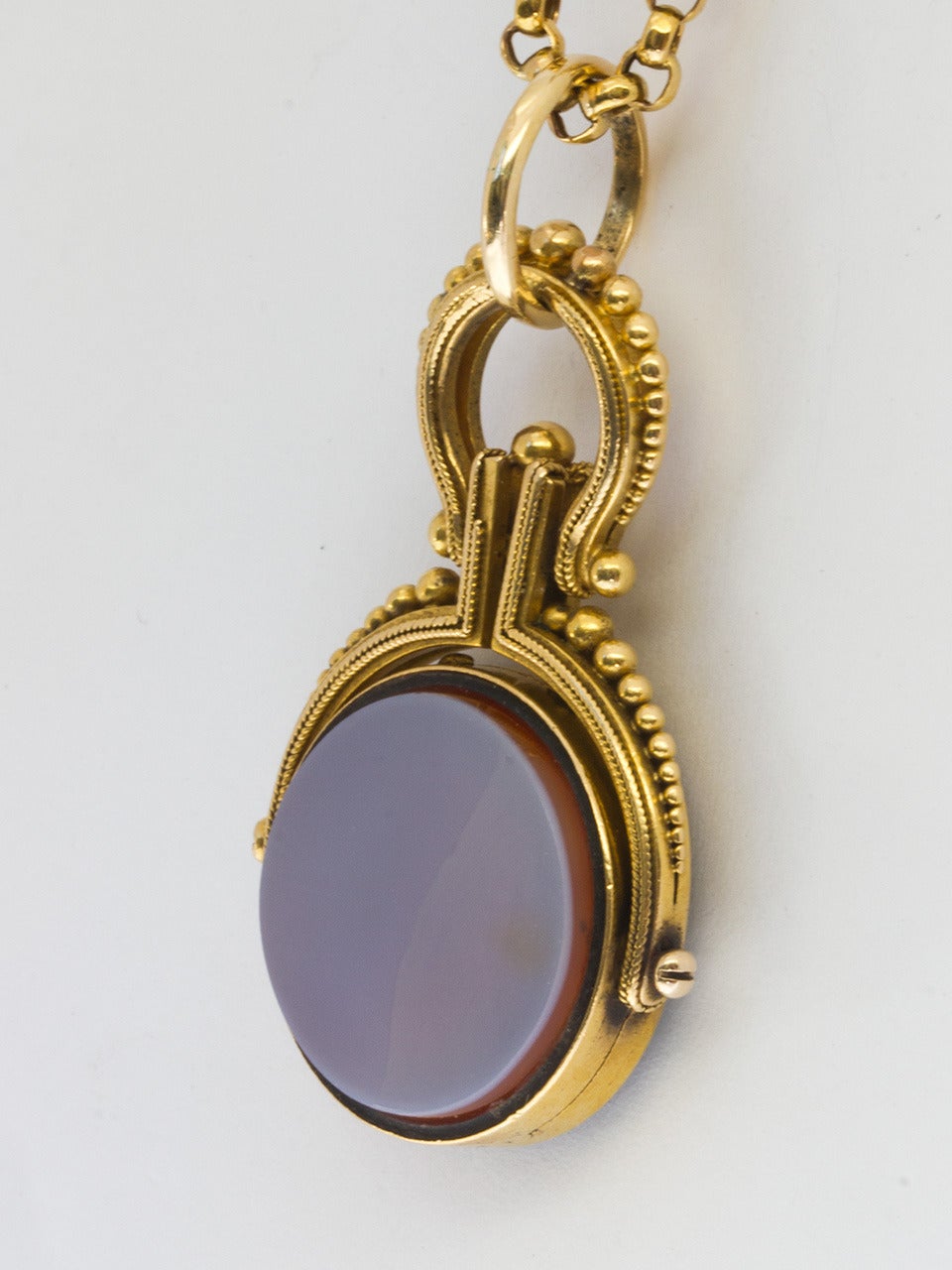 14K yellow gold antique spinner locket with bezel set hard stone carnelian on one side black onyx on the other. Substantial gold frame is decorated with fine braided trim and graduated size gold bead design. Worn on a beautiful round link antique 9K